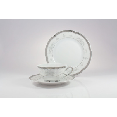 Zestaw herbaciany Ćmielów E361 Bolero Vera: biała porcelana ze srebrnym zdobieniem, filiżanka na spodku oraz talerz deserowy ustawiony pionowo w tle.