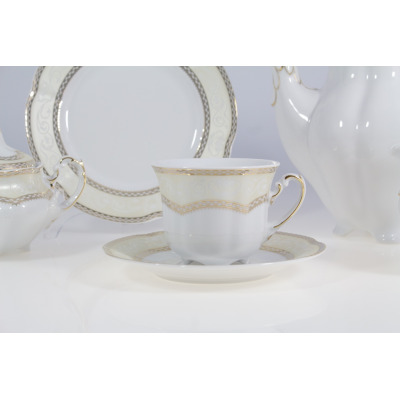 Elegancka filiżanka ze spodkiem z zestawu kawowego Ćmielów E363 Bolero Vienna. Biała porcelana ze złotym zdobieniem i kremowym wzorem, widoczna na tle serwisu.