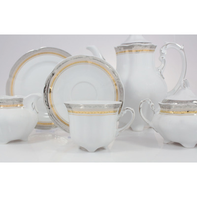 Zestaw do kawy Ćmielów E551 Bolero Princess. Biała porcelana ze złotymi i srebrnymi zdobieniami, obejmująca filiżankę, spodek, dzbanek oraz cukiernicę.