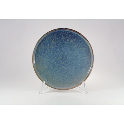 Talerz płytki Verlo Deep Blue o średnicy 28,5 cm na przezroczystym stojaku. Ceramiczne naczynie w odcieniach głębokiego błękitu z charakterystyczną kropkowaną