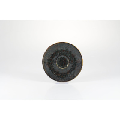 Okrągły spodek Fine Dine Jersey brown o średnicy 13 cm. Ceramiczne naczynie w odcieniach brązu i czerni z nakrapianą, nieregularną teksturą i wyraźnym