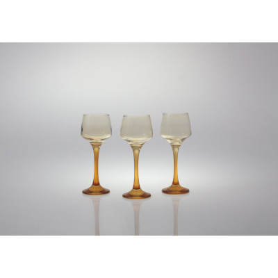 Trzy kieliszki do likieru 75 ml Sunset Miodowy marki Glasmark ustawione w rzędzie na białym tle. Szklane naczynia o smukłych, miodowych nóżkach i