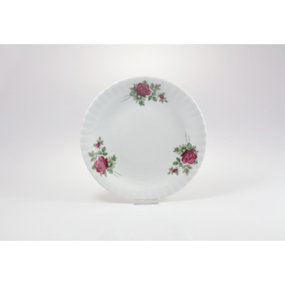 Talerz deserowy 21 cm Chodzież Iwona B826 z białej porcelany o falistym brzegu, ozdobiony motywem bordowych róż z zielonymi liśćmi, widok z góry na podstawce.