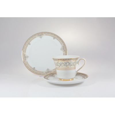 Porcelanowy zestaw kawowy Ćmielów G670 Margaret. Elegancka filiżanka na spodku z subtelnym, złotym zdobieniem i ornamentem roślinnym, w tle ustawiony ozdobny