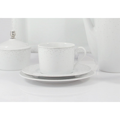 Biały zestaw do kawy Ćmielów G856 Jenny z subtelnym, kropkowanym wzorem. Zbliżenie na filiżankę ze spodkiem, obok cukiernica i dzbanek z porcelany w eleganckim