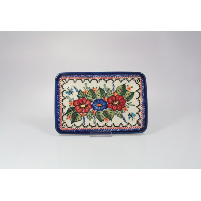 Prostokątna tacka ceramiczna Bolesławiec 149AR o wymiarach 18,3 x 12,3 cm. Kremowe tło zdobi ręcznie malowany wzór z czerwonymi i niebieskimi kwiatami oraz